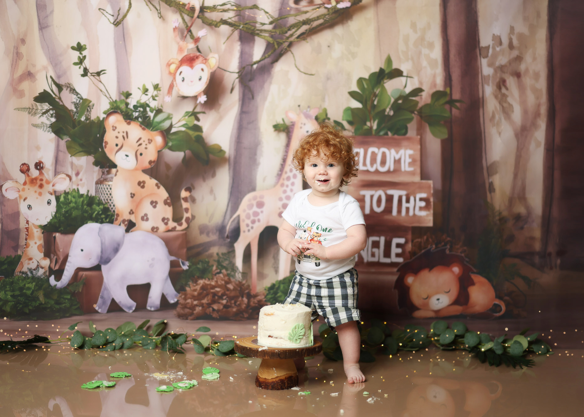 Toddler boy enjoying a jungle-themed animal smash cake during a first birthday photoshoot in a studio.