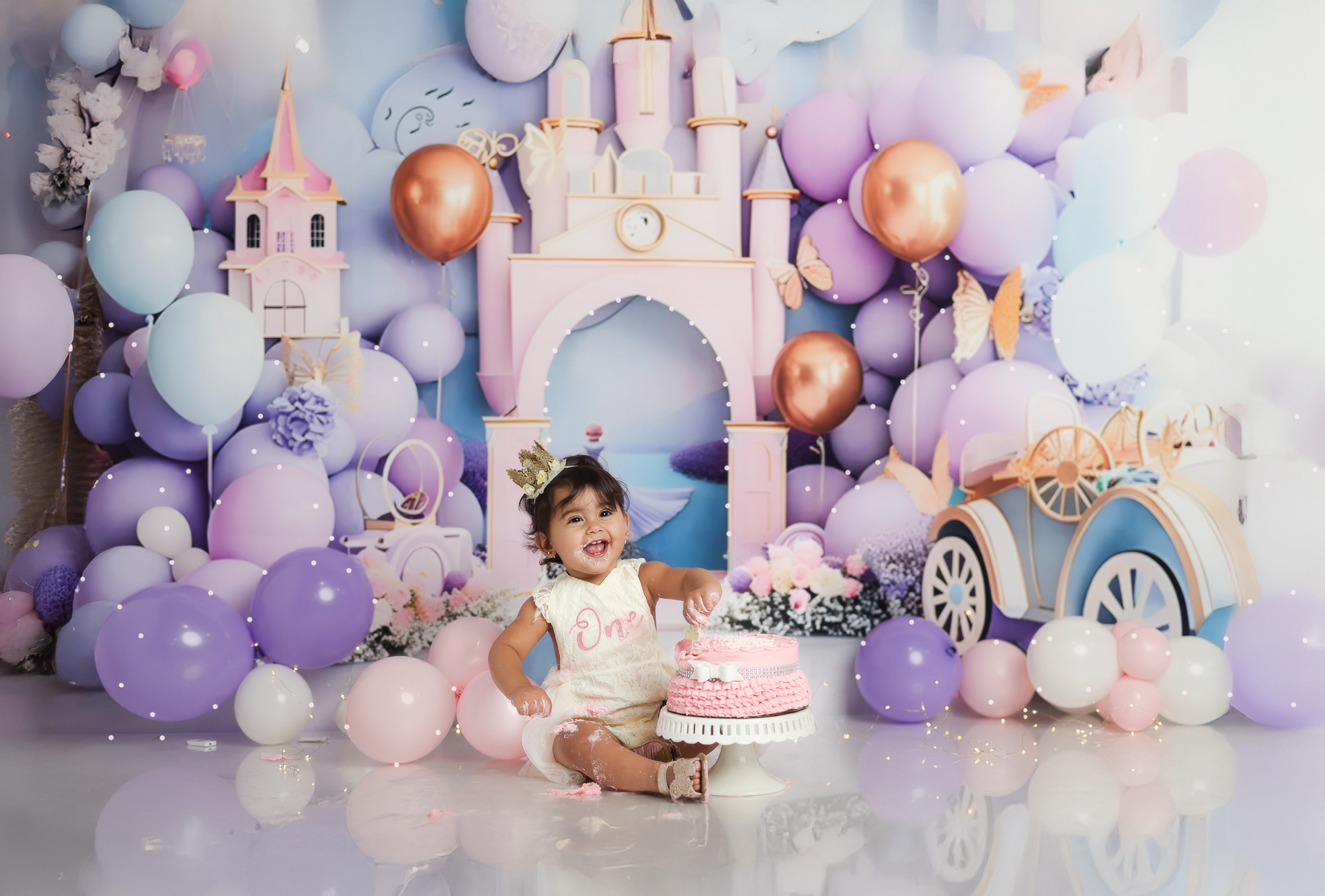 Toddler dressed as a princess enjoying a birthday smash cake in a photography studio during a first birthday photoshoot.